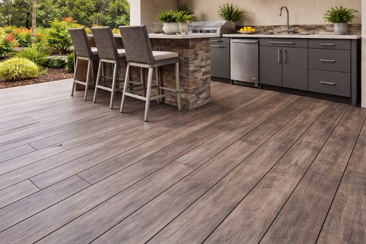 All weather outdoor kitchen with composite floor boards, stacked stone island, stainless appliance, and modern storage cabinets