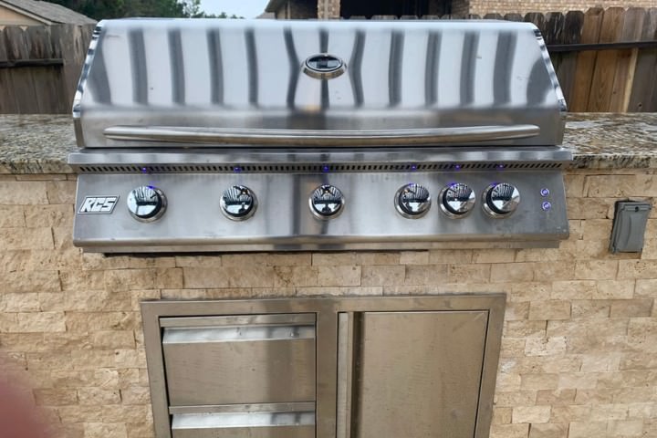 Built-in stainless grill with stone base showing a classic outdoor kitchen material combination