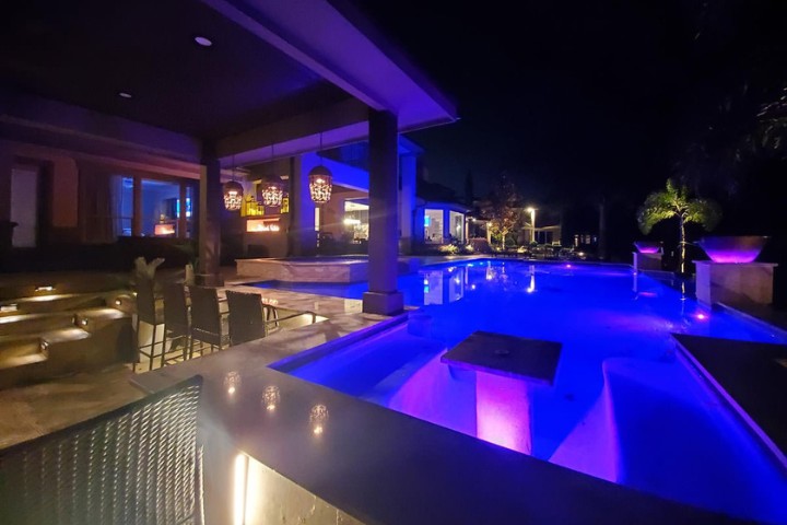 Automated underwater pool lights brighten the swim area near a covered patio