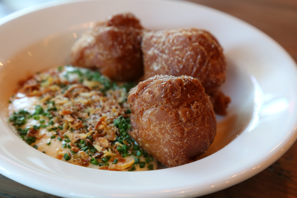 The loaded baked potato beignets are light, airy puffs sitting atop a potato and cheddar mousseline finished with fried onions, ham dust and chives.