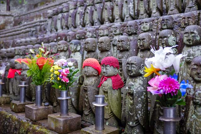 Small statues of Japanese people, a couple of which wearing knitted caps with artificial flowers in the foreground