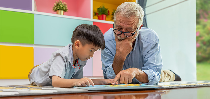 An elderly man reading with a preschool age boy.