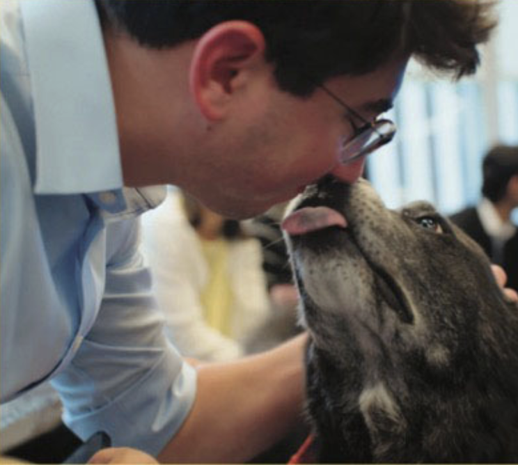 Photo is person with white skin getting a kiss from a black dog. 