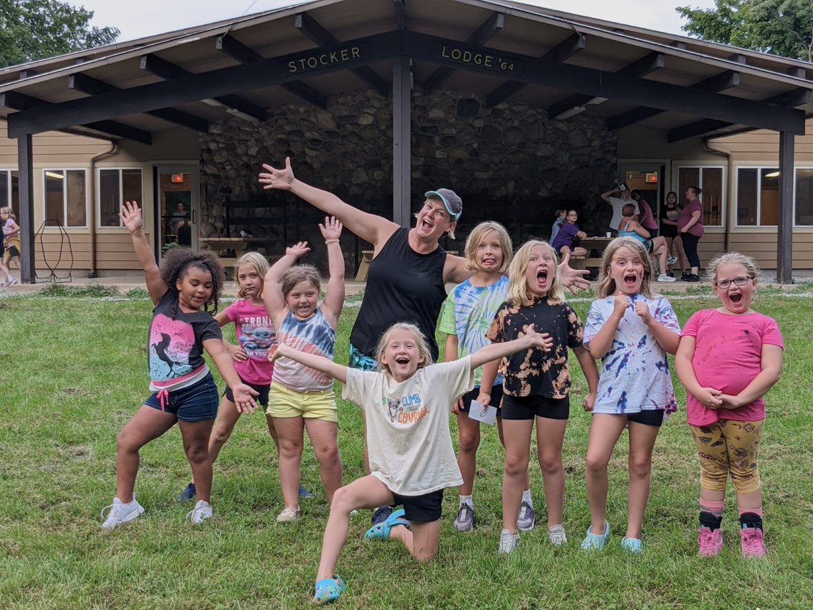 Group of girls with troop leader standing outside of Stocker Lodge at Timberlane. All girls are excited since it was their first time camping!