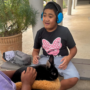 Boy with ear coverings petting rabbit