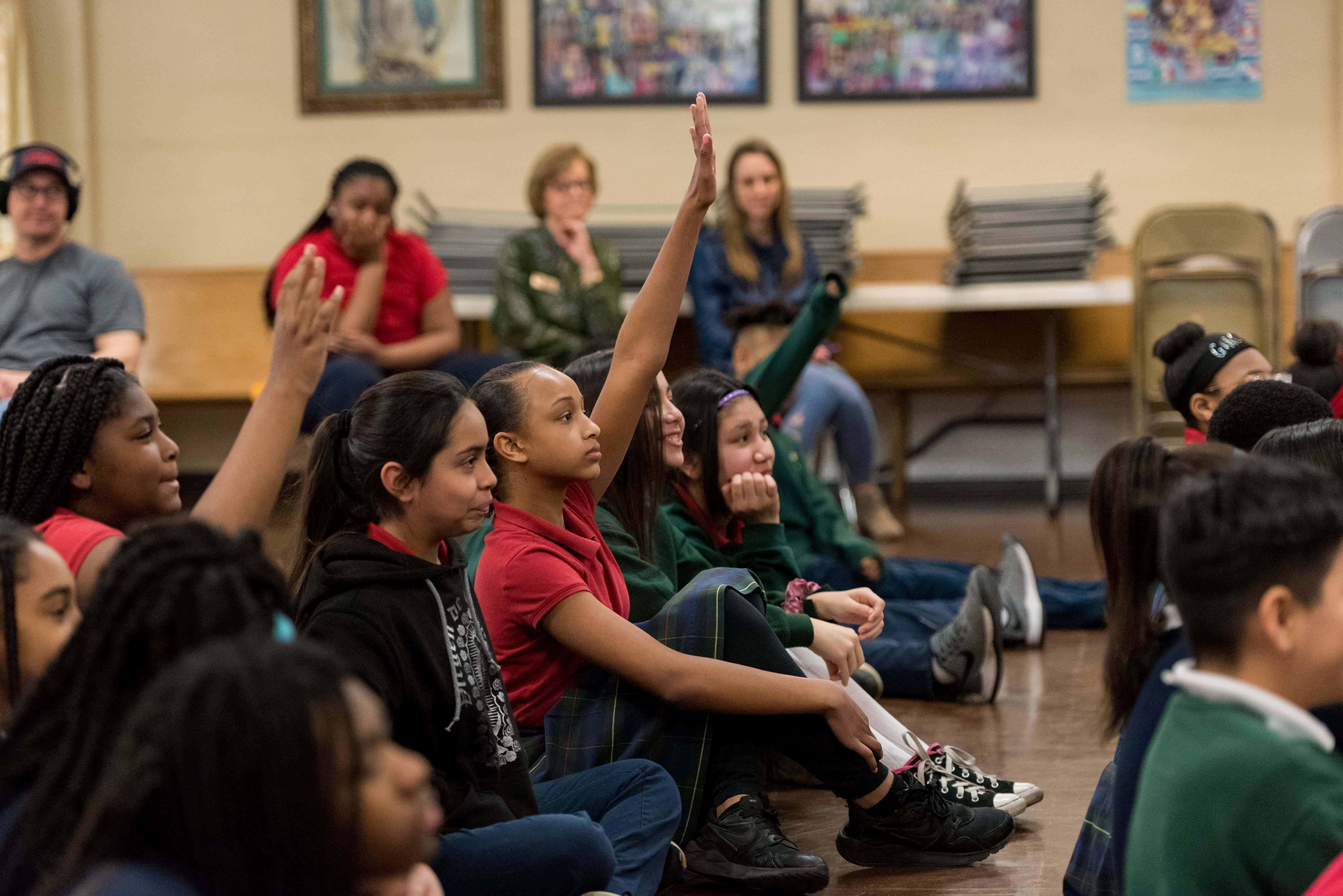 Image of student raising her hand to answer a question.