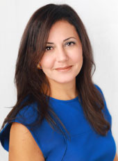 Heather Ibrahim-Leathers is smiling demurely at the camera, her long brown hair falls behind her and she's wearing a blue dress.