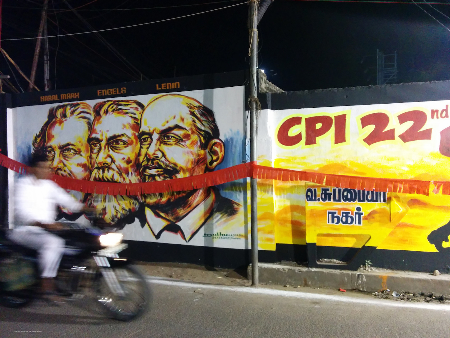 Man on motorcycle drives past communist street art