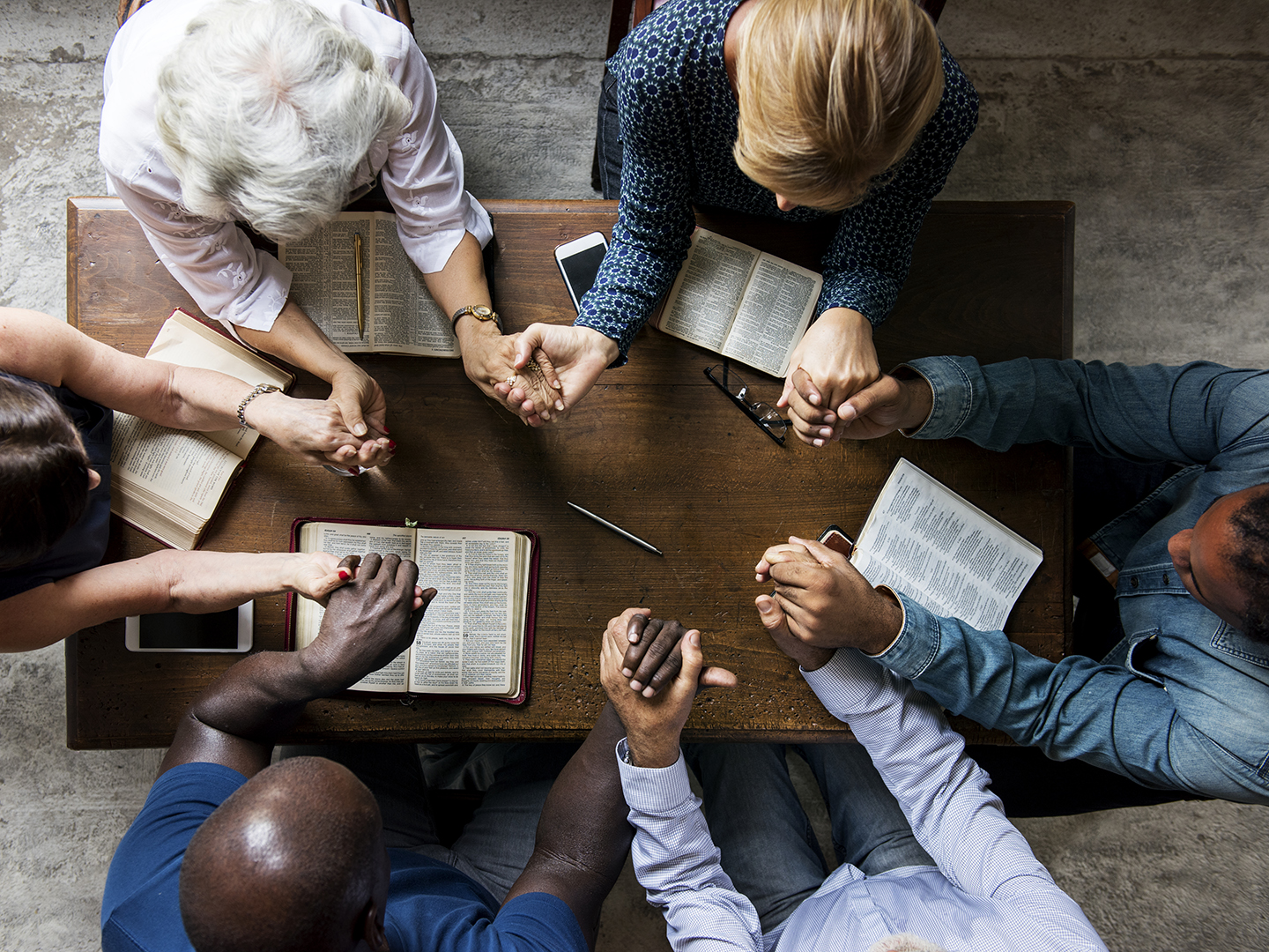 Group of diverse people holding hands around a table with Bibles