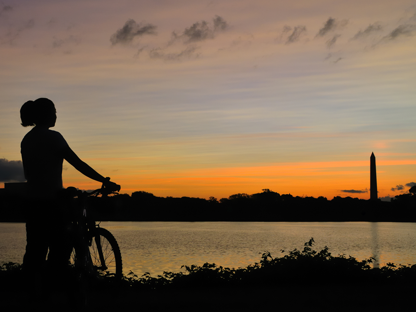 Young woman standing next to her bike at sunset overlooking the Washington Monument in Washington, DC