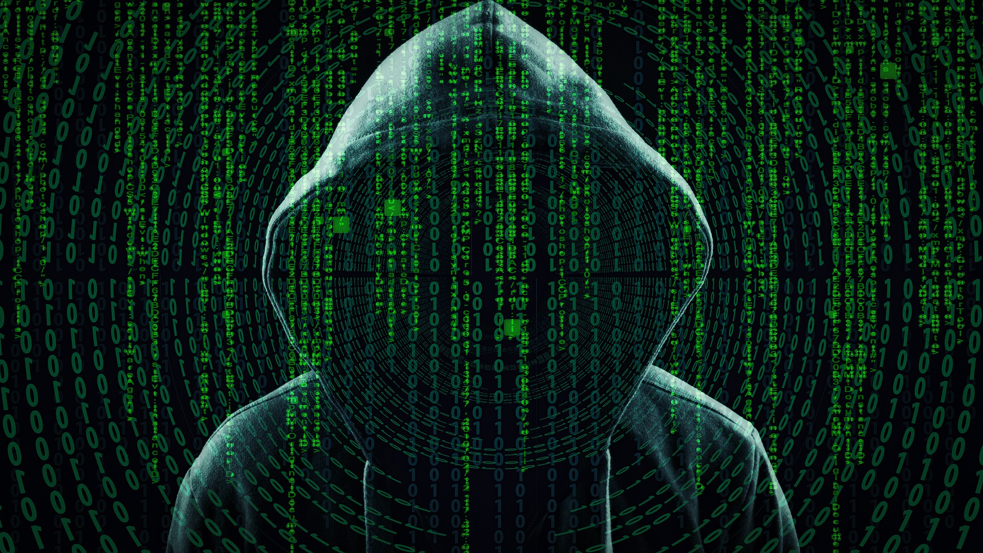 A photo of a hacker in the shadows with a black hoodie, and green binary number codes