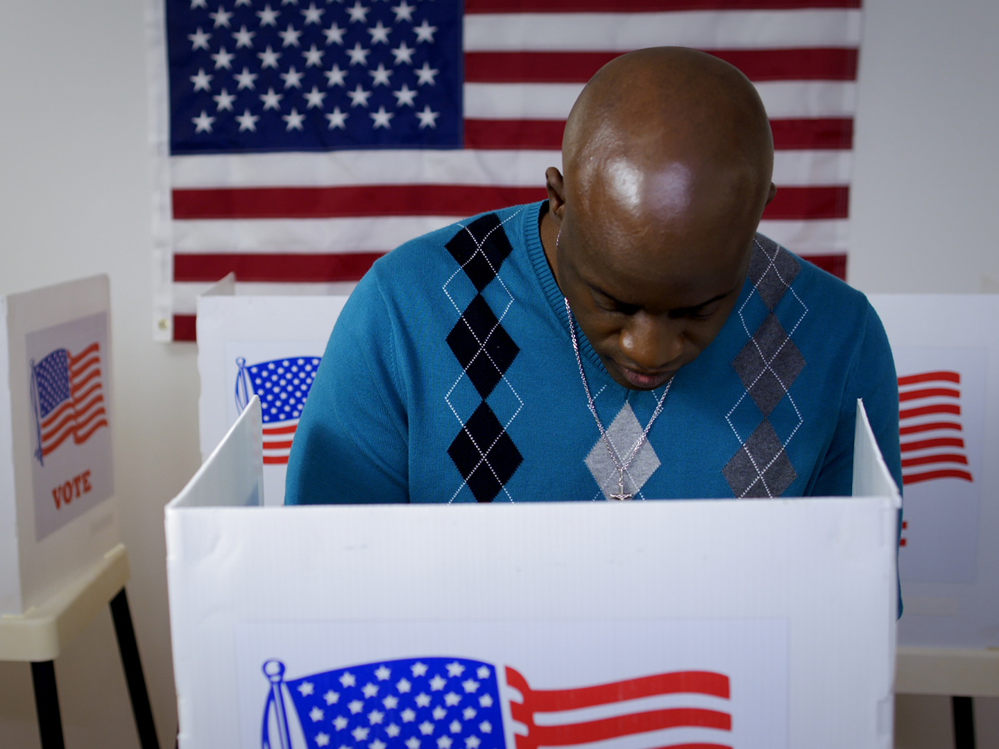 A man stands in a voting booth marked with the USA flag