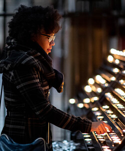 A young Black woman lights a candle in a church