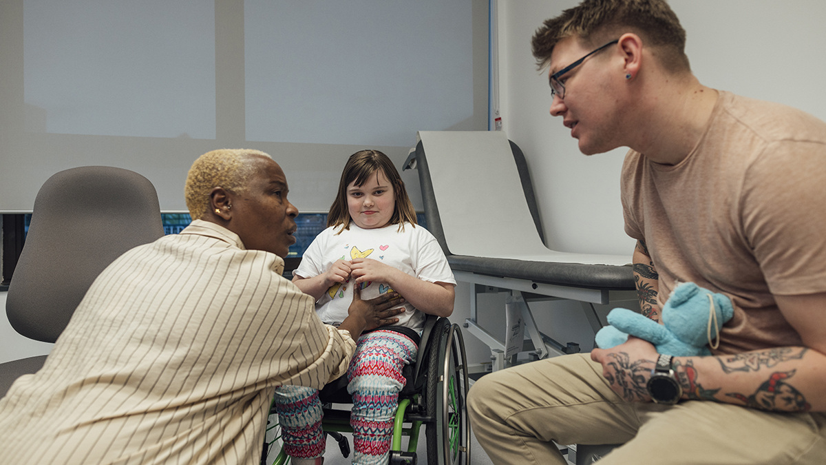 A young girl in a doctor's office with her father and a female doctor during a routine medical visit.