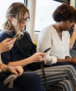 Four people sit in a subway train car looking at their phones.