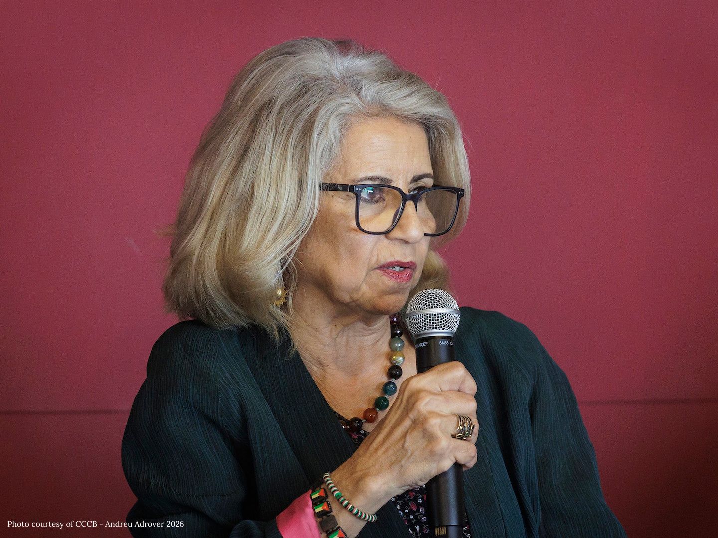 Ahdaf Soueif speaks into a microphone in front of a red wall