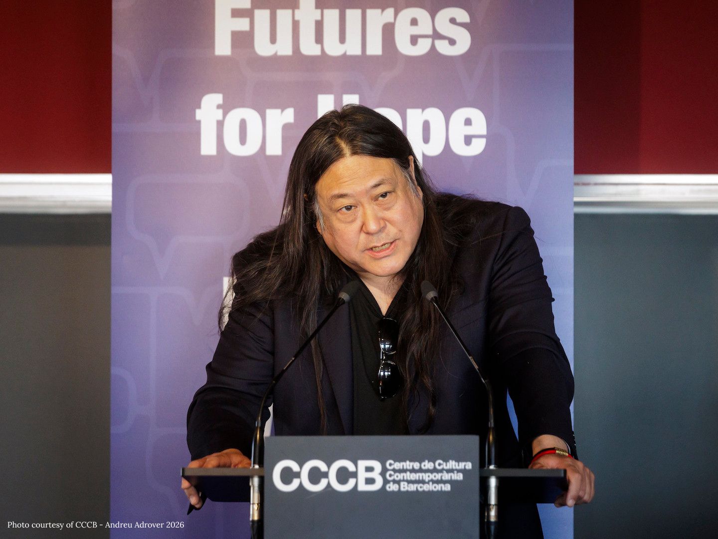 Kaiser Kuo speaks at a podium with signs that read "Futures for Hope" and "Centre de Cultura Contemporània de Barcelona"
