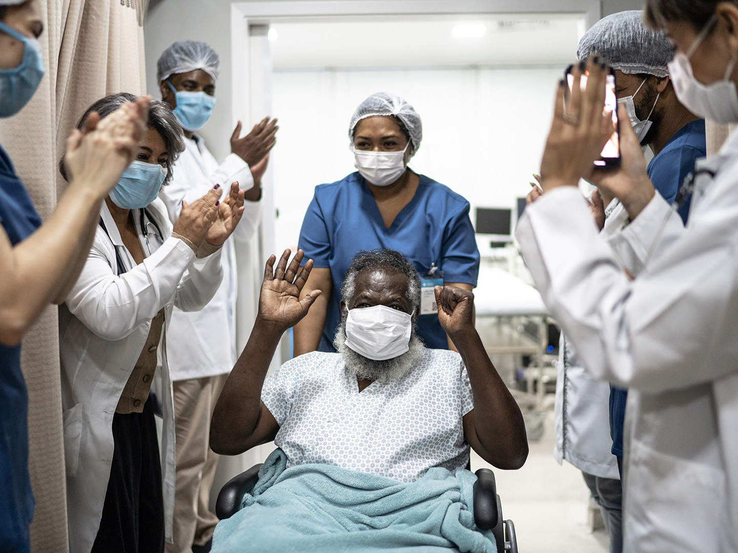 Doctors and nurses celebrating senior man leaving the hospital after recovery - wearing protective face mask