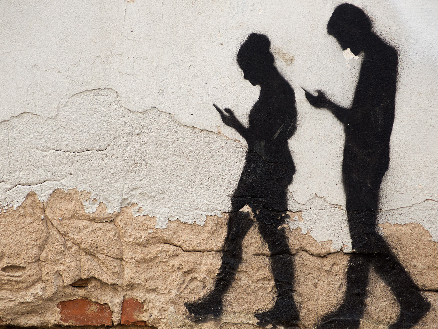 Street wall art of pair of young people walking while looking to mobile phone screen