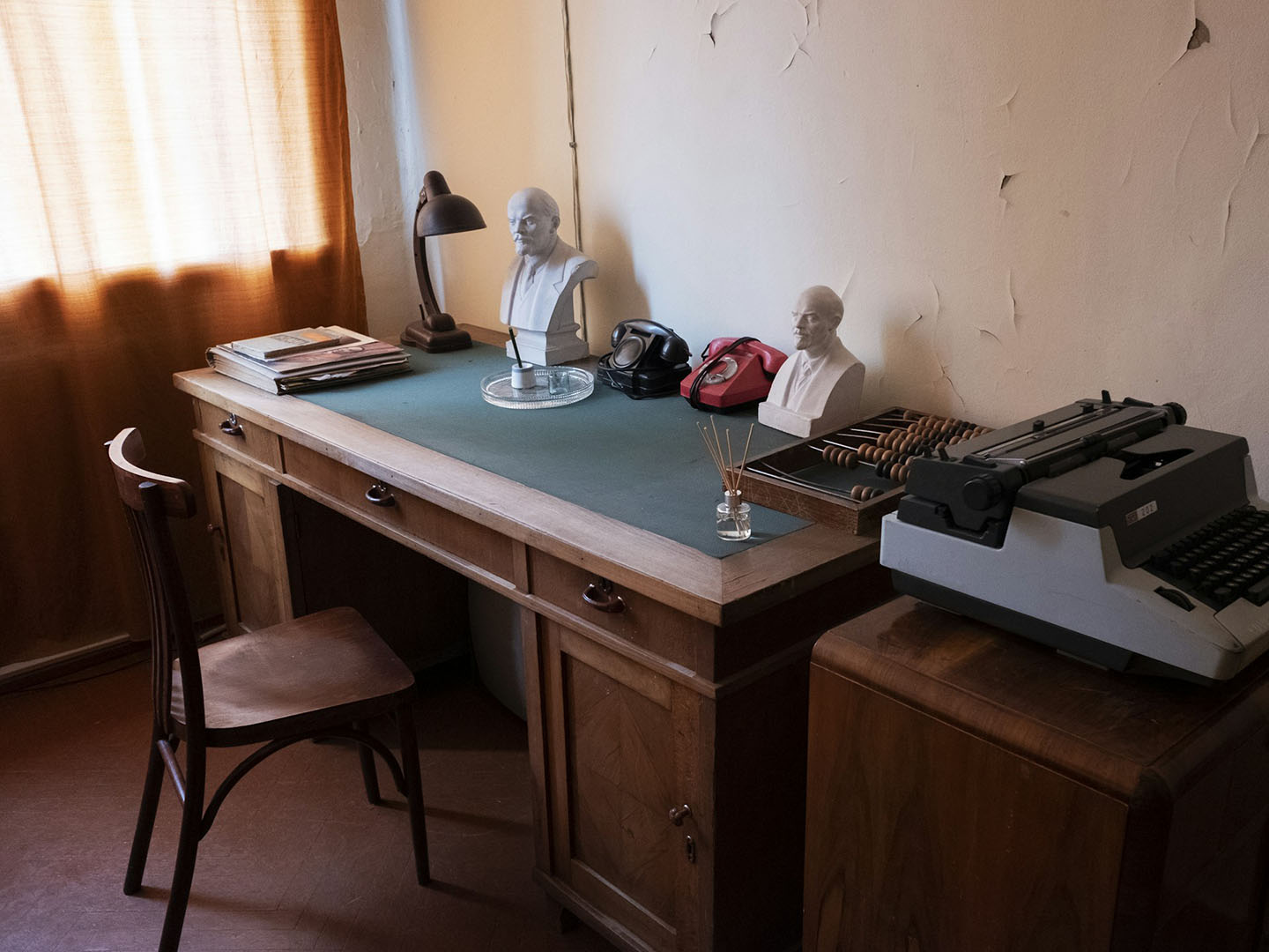 Old wooden desk and chair topped with small statues of Lenin, a typewriter, and rotary phones