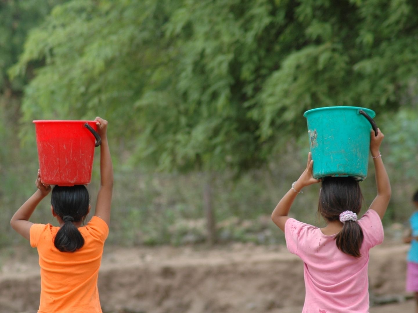 Two young girls carry buckets on their heads in Bolivia.