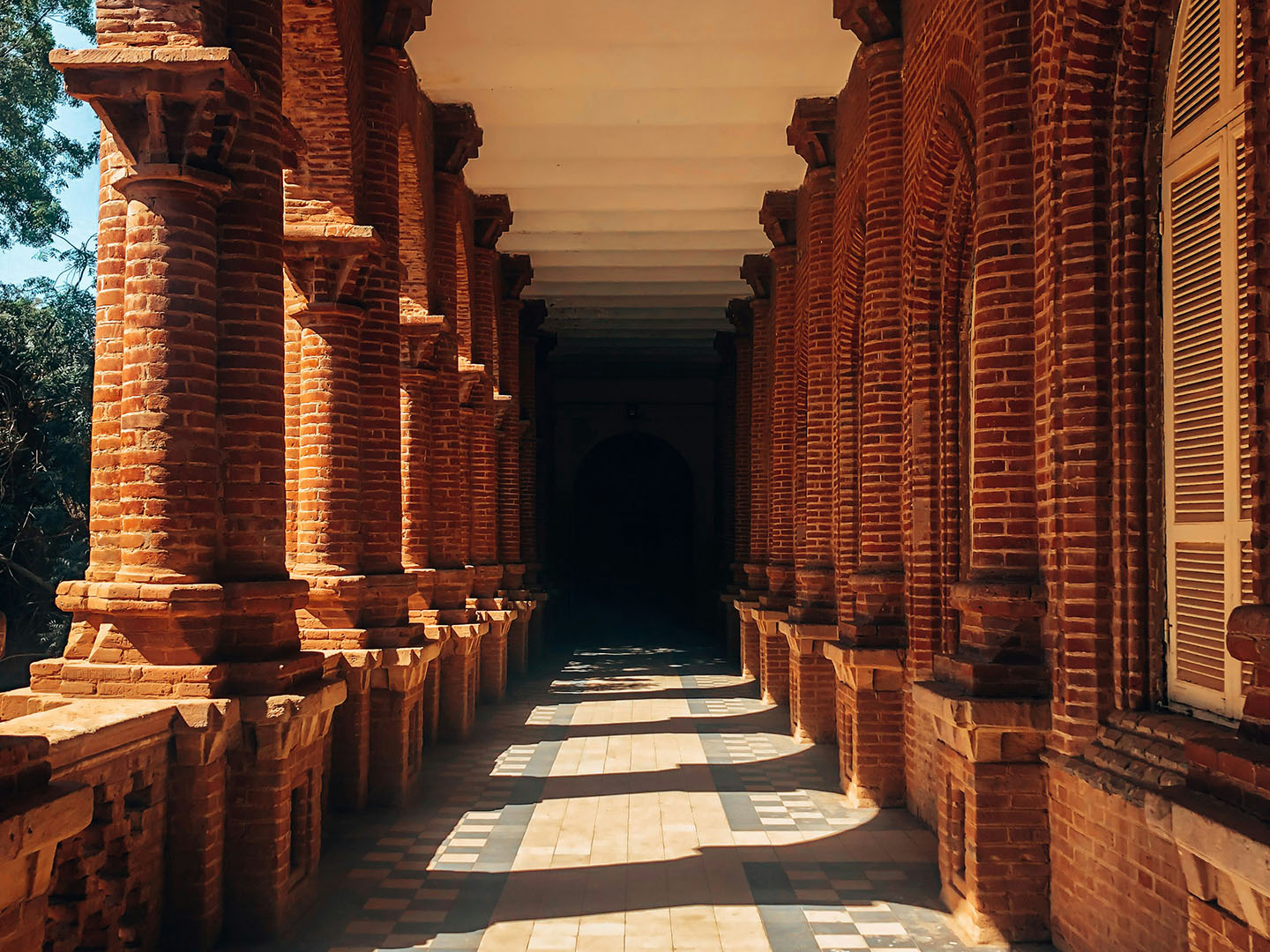 Sun shining into an outdoor hallway with brick columns and a blue-and-cream tiled floor at the University of Khartoum