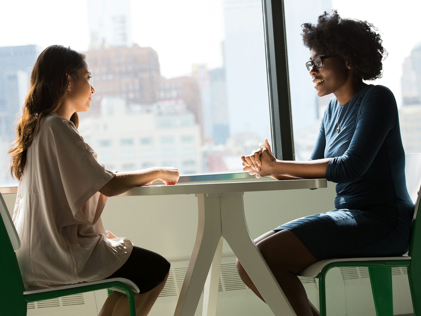 Two women sitting at a table facing each other and talking