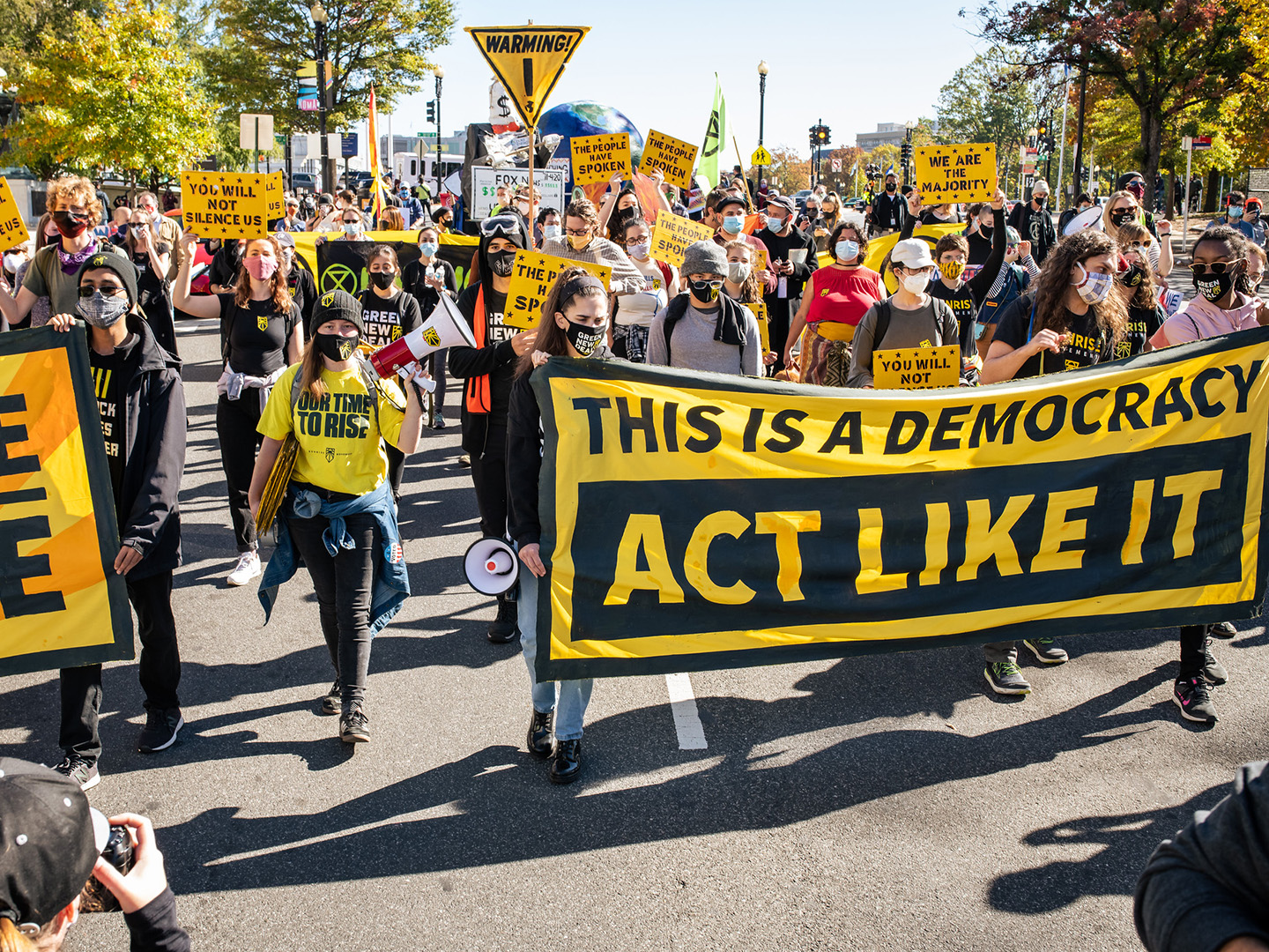 A protest with a sign that reads "This is a Democracy, Act Like It"