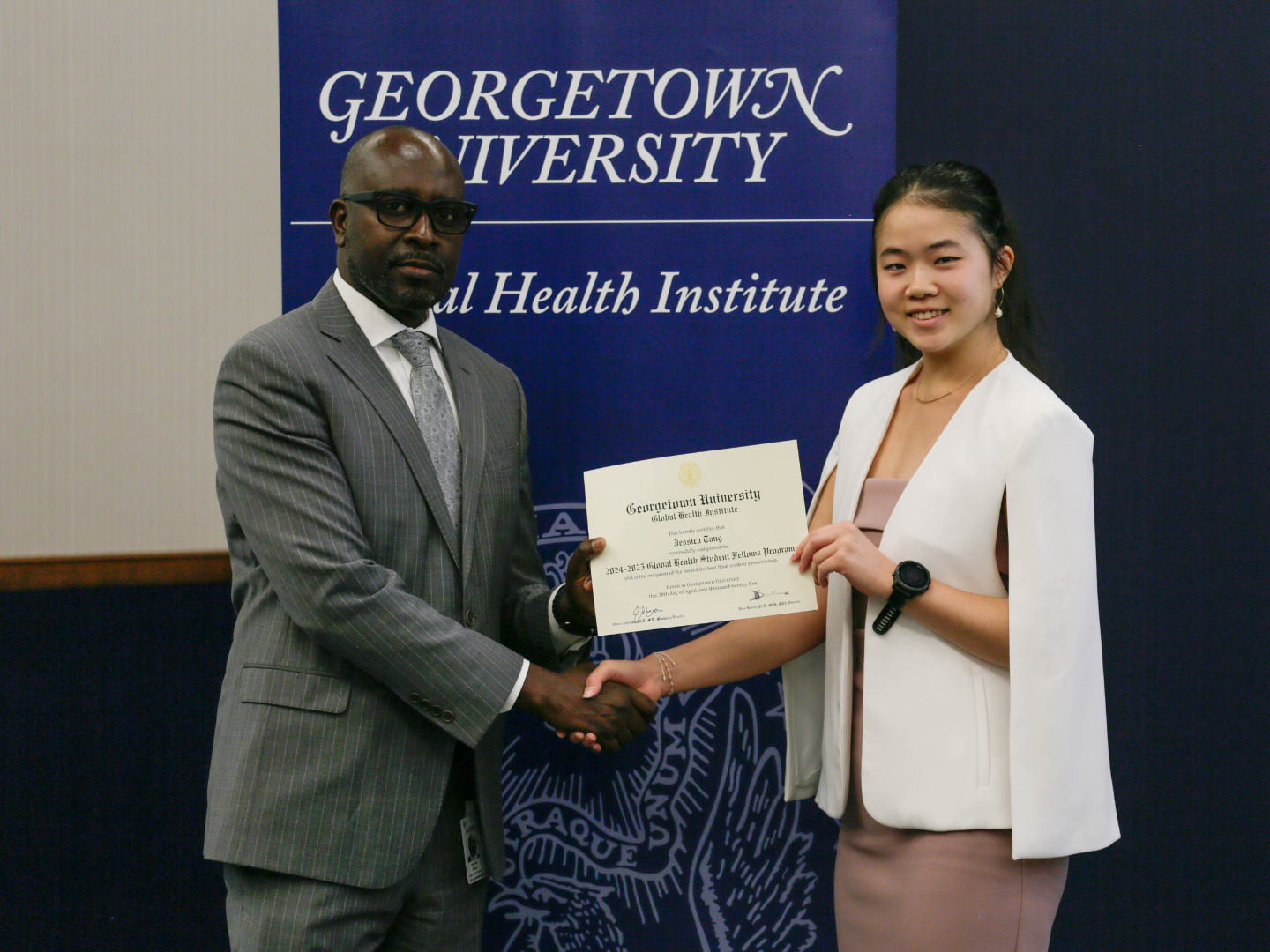 Global Health Institute Director Deus Bazira hands certificate of completion to Student Fellow Jessica Tang