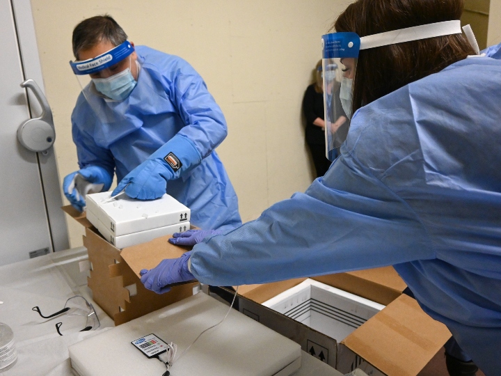 Two workers in PPE package vaccines in boxes