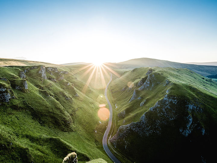 Road between two grassy cliffs ends in a sunrise