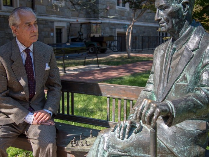 Actor David Strathairn sitting on a bench on Georgetown's campus, next to a sitting statue of Jan Karski.