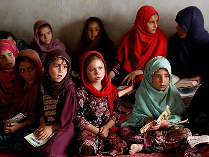 A group of young Afghan girls sitting together with books in their laps.
