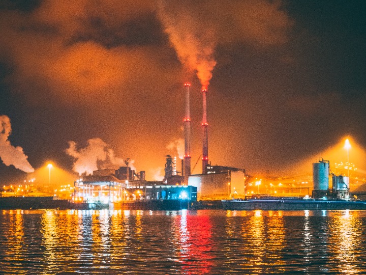 Factory on a waterfront producing smoke, pollution gives the night sky an orange glow.