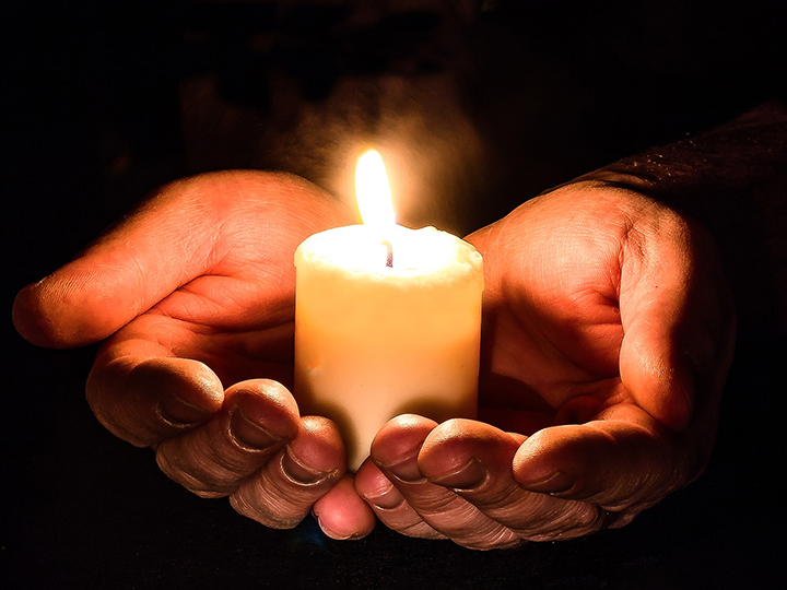 A close-up of someone holding a lit candle in the palm of their hands.