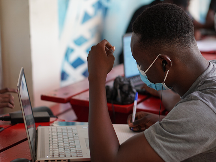 A man wearing a mask to protect against COVID-19 while working on a laptop in an internet cafe in Ghana