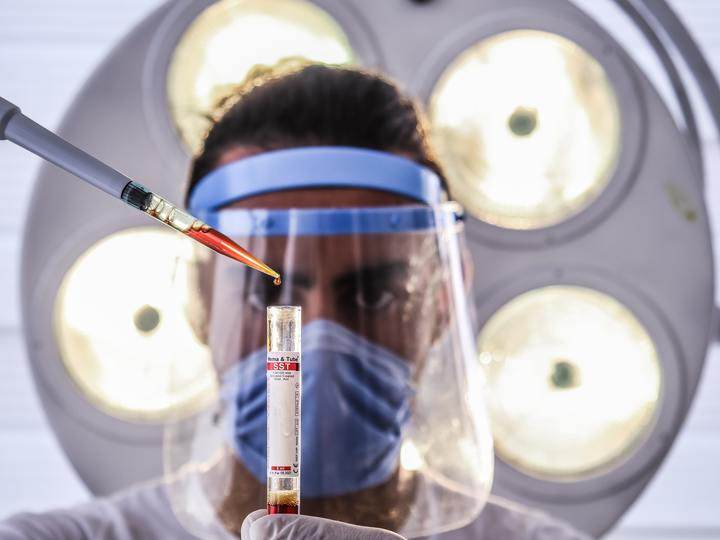 A scientist wearing a mask and face shield conducts research about COVID-19