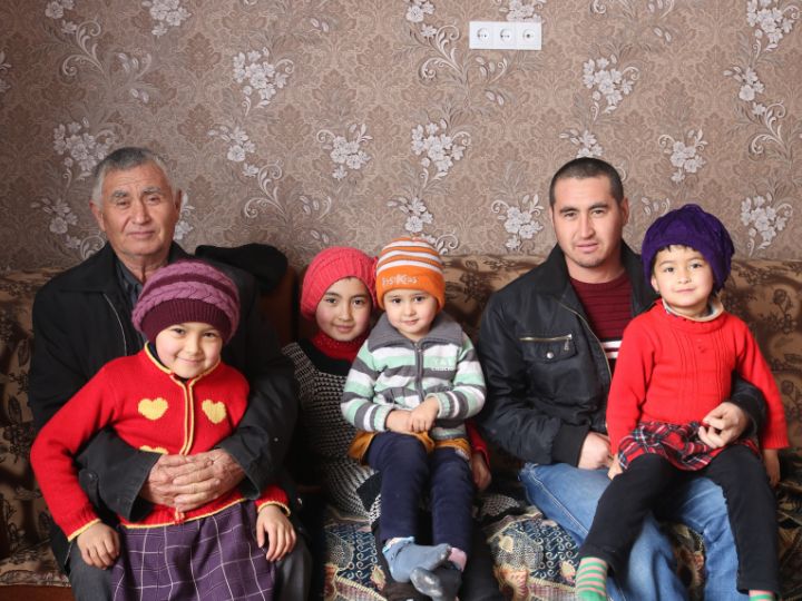 Two men and four children sitting on a couch and smiling in Central Asia.