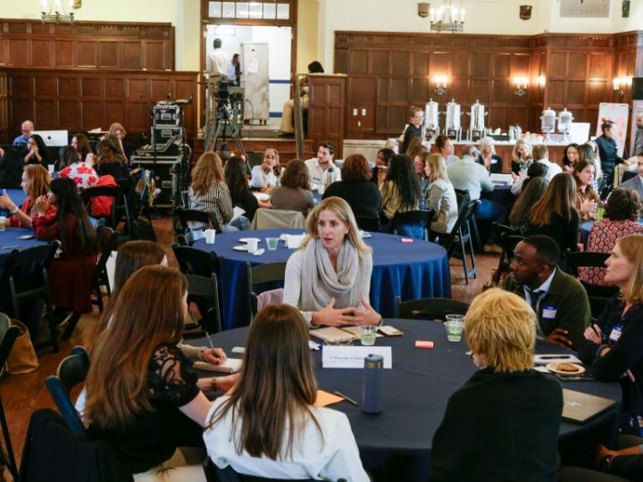Dozens of attendees sit in round tables in Copley Formal Lounge