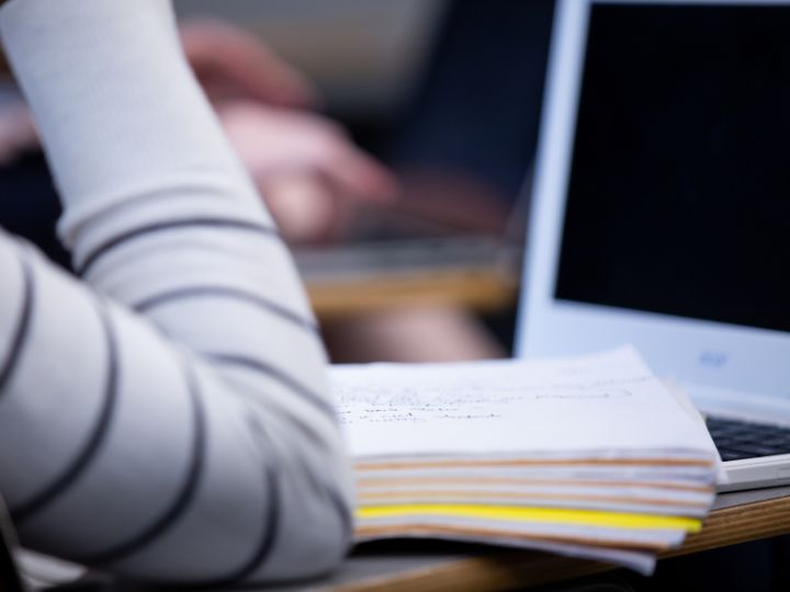 A desk with a notebook, computer, and student's arm