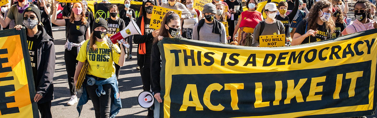 A protest with a sign that reads "This is a Democracy, Act Like It"