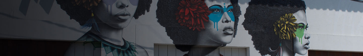 Mural en Colombia representando a tres afro latinas con flores en las orejas y pintura en los ojos