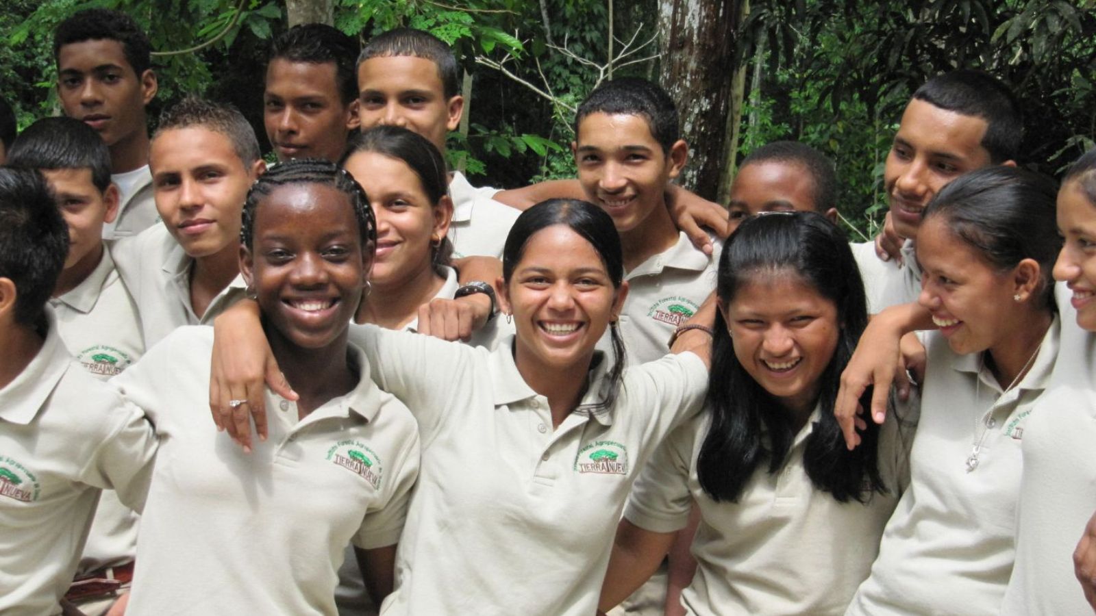 A dozen teenagers stand arm in arm, smiling