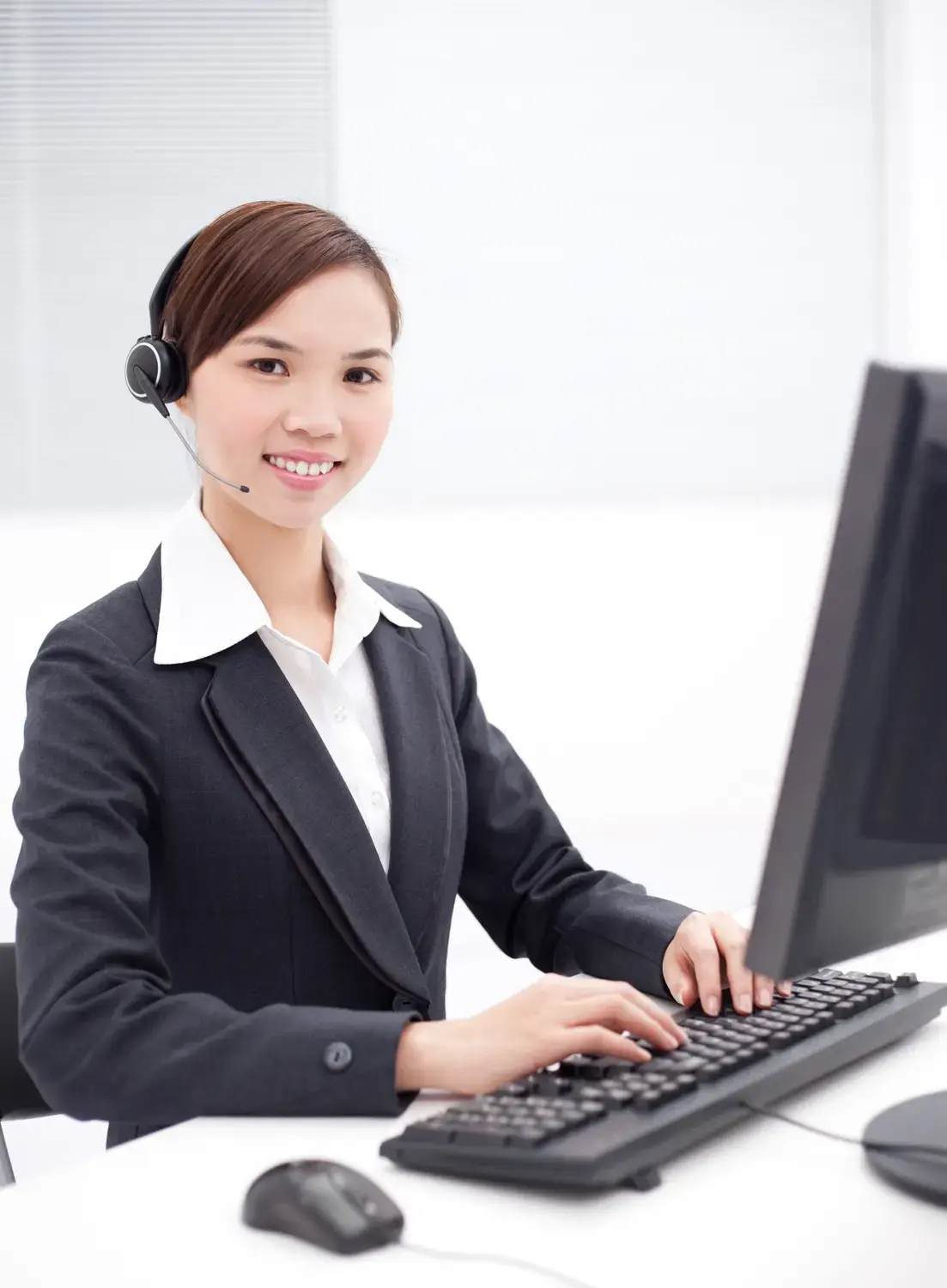 A friendly customer service representative answering calls for a small business using a headset and computer.