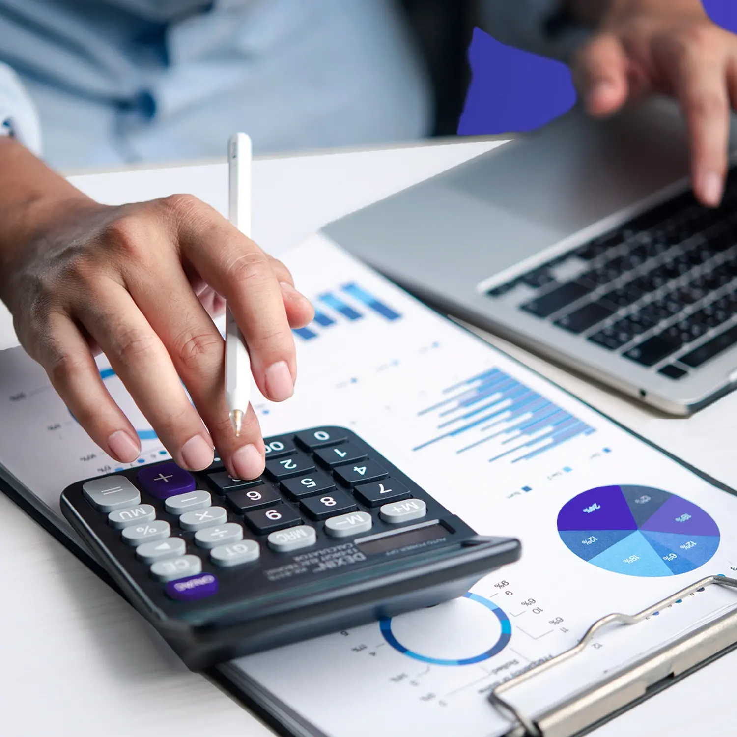 Hand using a calculator over business charts next to a laptop, representing year-end planning, budgeting, and forecasting.