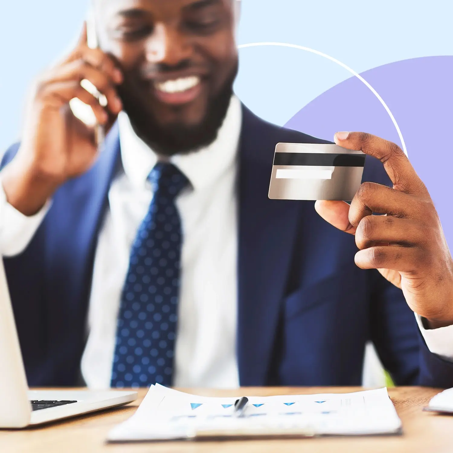 Person on a phone call holding a credit card at a desk with a laptop and paperwork, representing phone payments and PCI security.