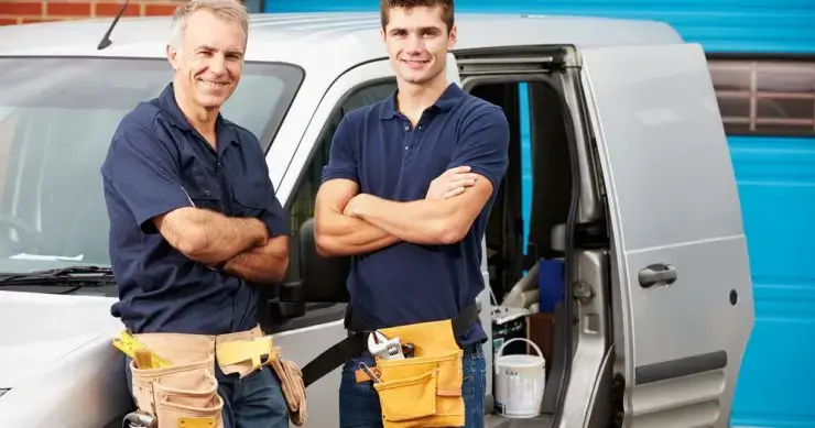 Two plumbers standing beside their van