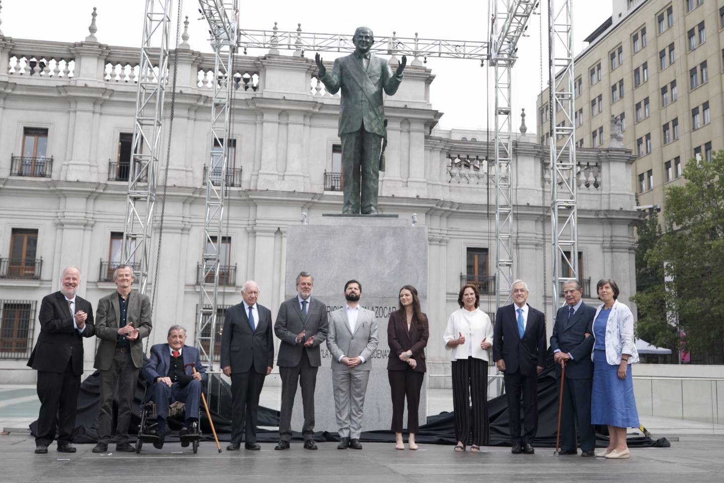 Fotografía del Presidente Gabriel Boric e Irina Karamanos, acompañado de familiares de Patricio Aylwin y los ex Presidentes Ricardo Lagos y Sebastián Piñera, con la estatua de Patricio Aylwin de fondo.