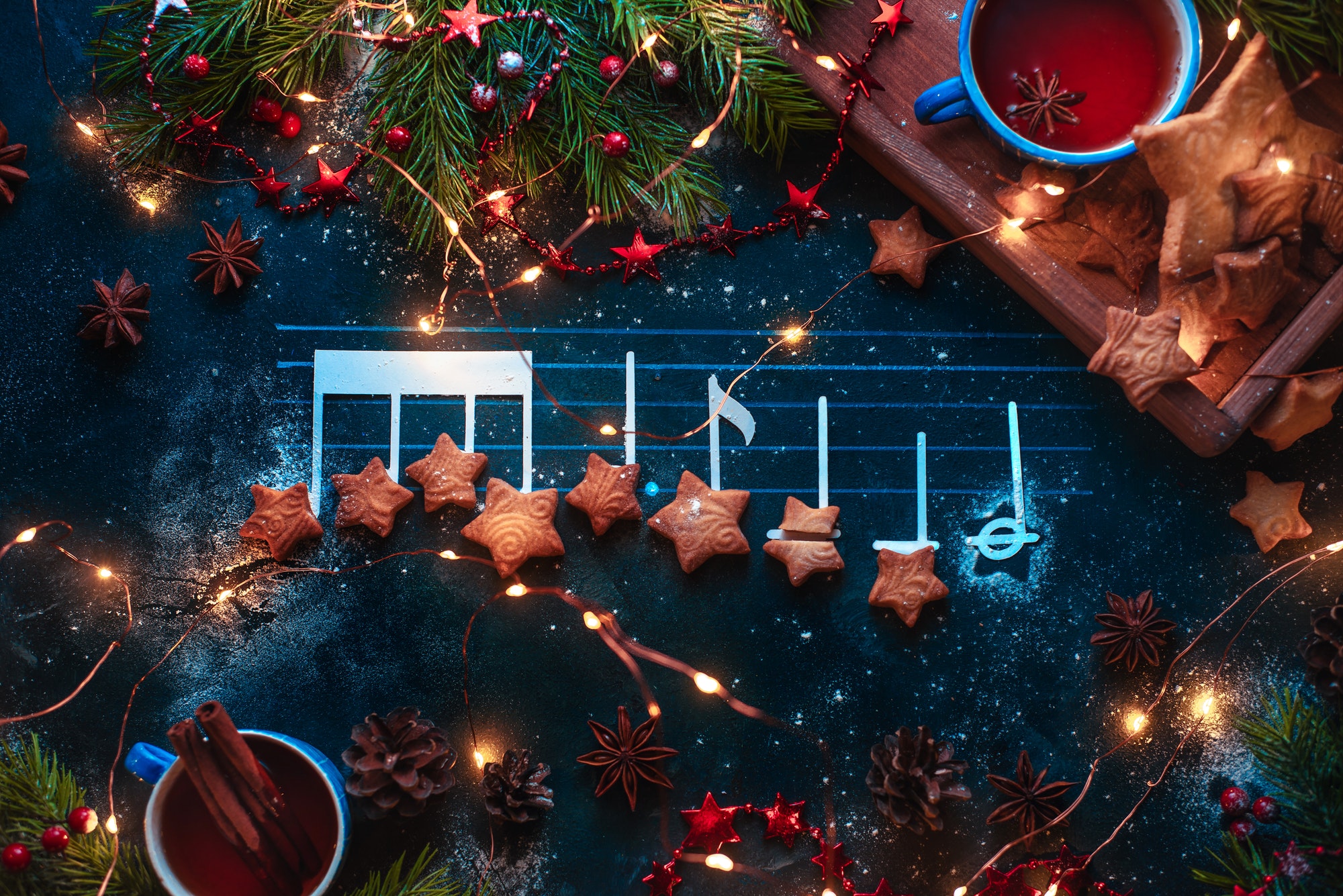 Christmas melody notes flat lay with star-shaped cookies, fir tree branches, wooden tray, anise