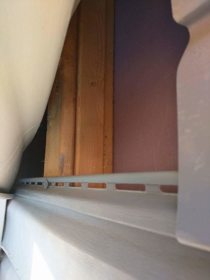 Spraying polyurethane over pink foam board on exterior wall under vinyl siding